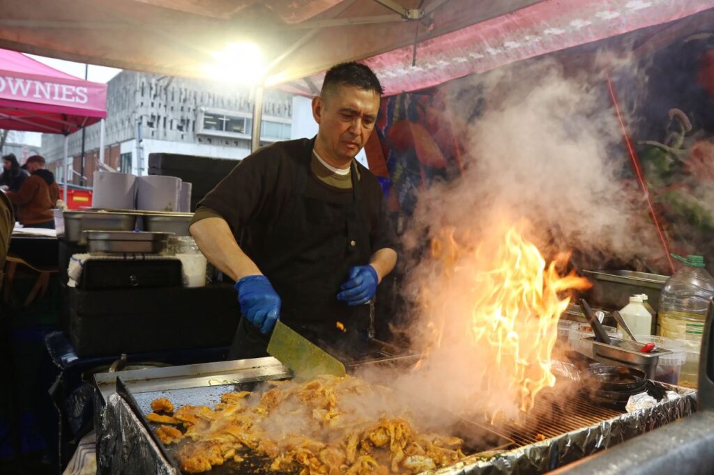 A man standing at a flaming grill cooking