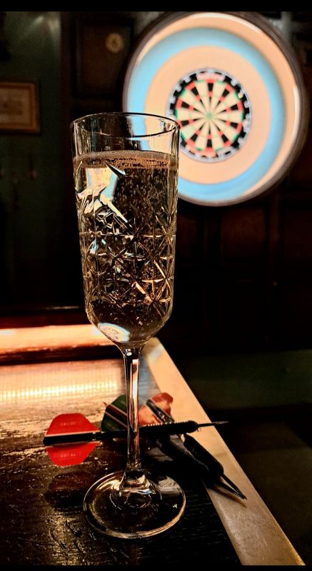 A glass of bubbly with a dart board in the background