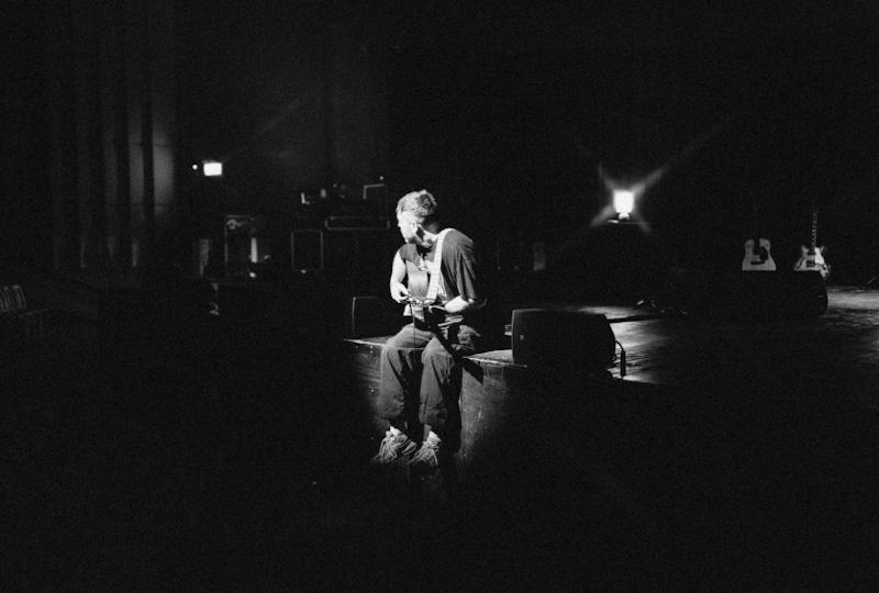 Benjamin Franics Leftwich performing on a stage. He is seated, playing a guitar while a spotlight focuses on him