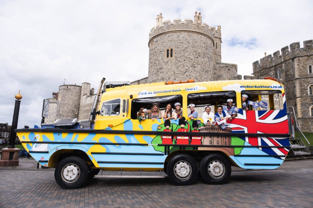 The cast of Dick Whittington, the 2024-25 pantomime at Theatre Royal Windsor on a duck boat with Windsor Castle in the background