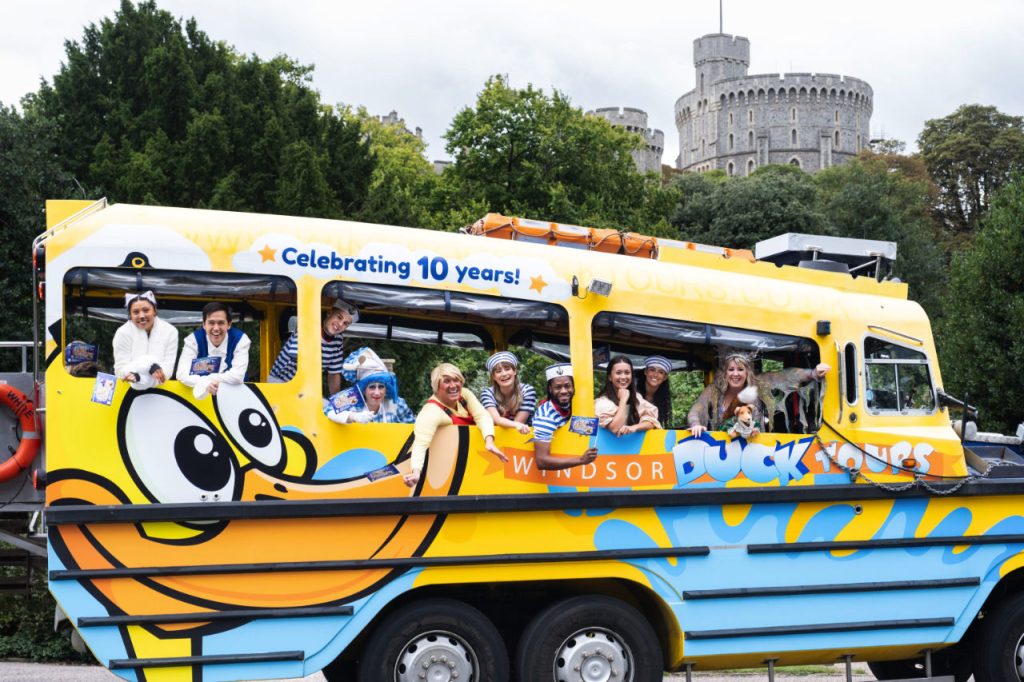 The cast of Dick Whittington, the 2024-25 pantomime at Theatre Royal Windsor on a duck boat with Windsor Castle in the background