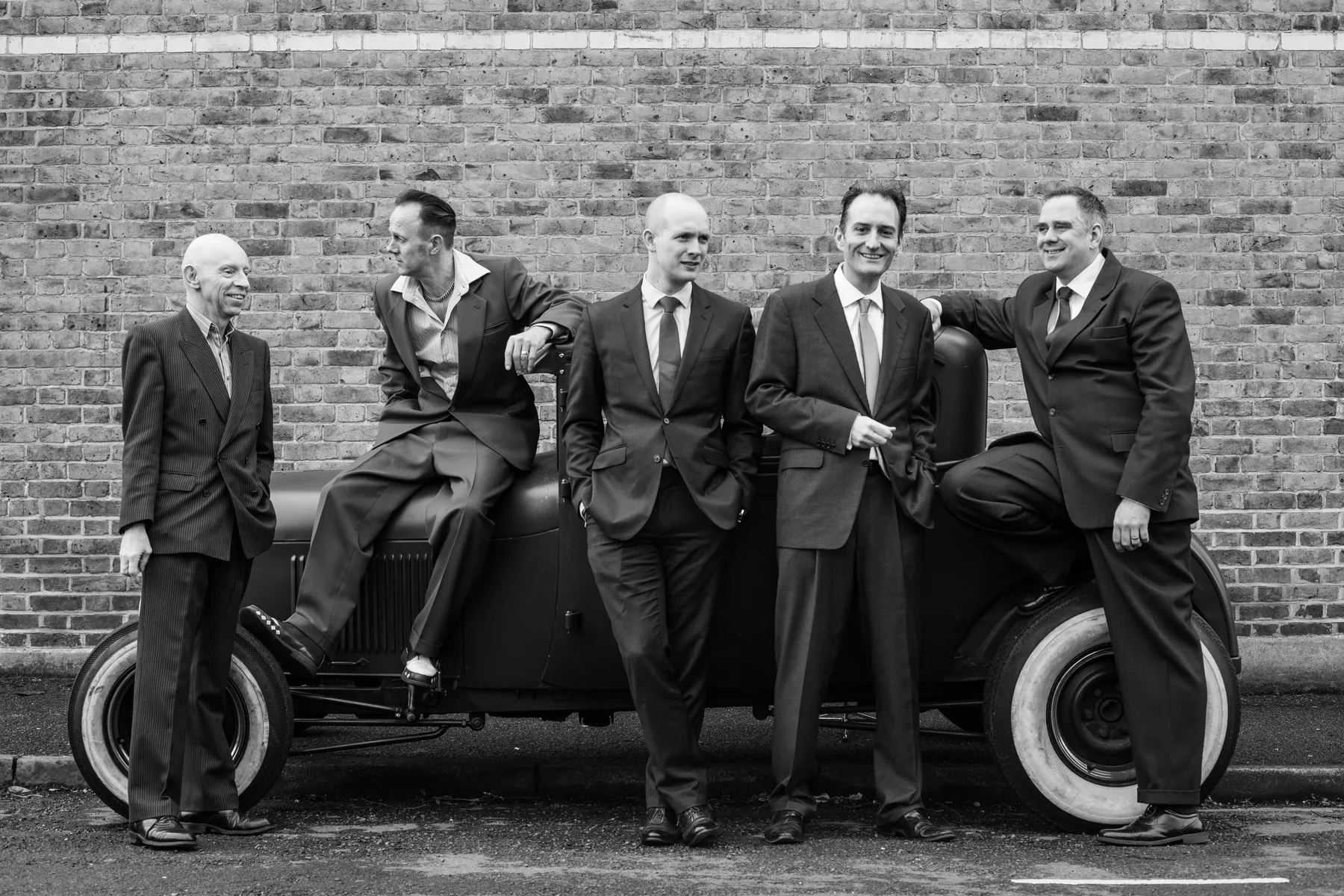 The band members of the Ding Dong Daddios sitting around a vintage car. The picture is in black and white