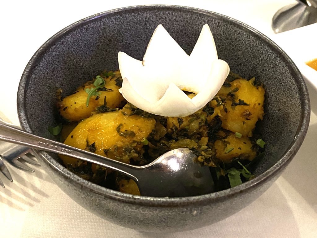 A bowl of Sag Aloo – potatoes with an onion crown