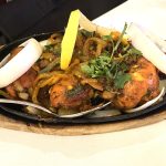 A plate of tandoori chicken topped with slices of raw onion and a lemon