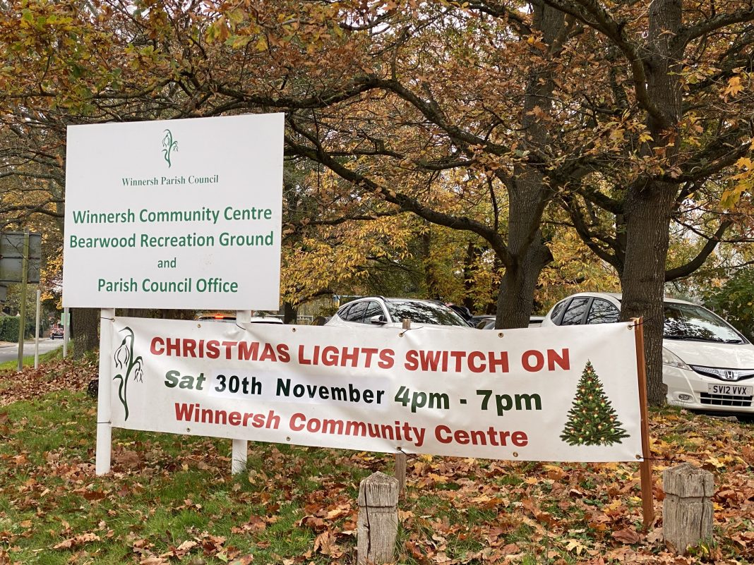 A banner promoting the launch of Winnersh Christmas lights, next to a sign at the entrance to Bearwood Recreation Ground. Behind the signs are tears shedding their leaves, which have turned orange and fallen on the ground. The banner reads: 