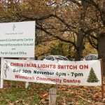 A banner promoting the launch of Winnersh Christmas lights, next to a sign at the entrance to Bearwood Recreation Ground. Behind the signs are tears shedding their leaves, which have turned orange and fallen on the ground. The banner reads: "Christmas light switch on, Sat 30th November 4pm - 7pm, Winnersh Community Centre'. The sign reads 'Winnersh Community Centre Bearwood Recreation Ground, and Parish Council Office'