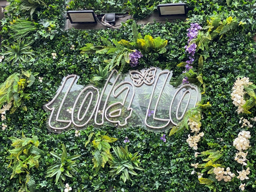 The sign to Lola Lo in Reading. It is lit up at night and surrounded by decorative foliage