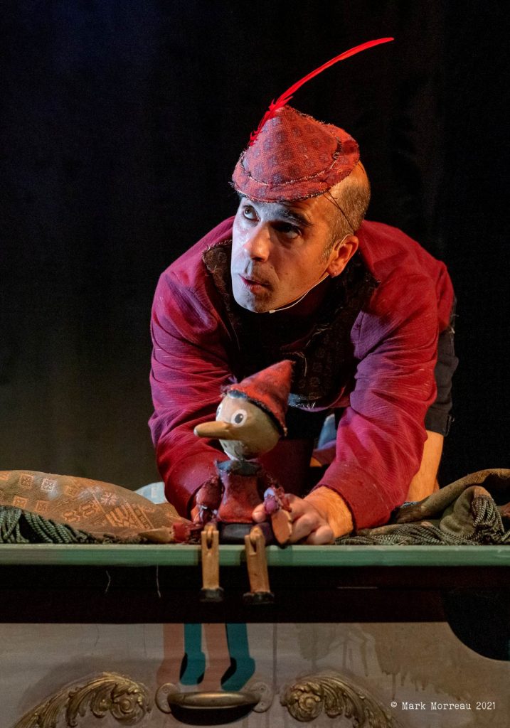 Actor Joss J. MacDonald playing Pinocchio holding a puppet of the same character. Both have red hats on