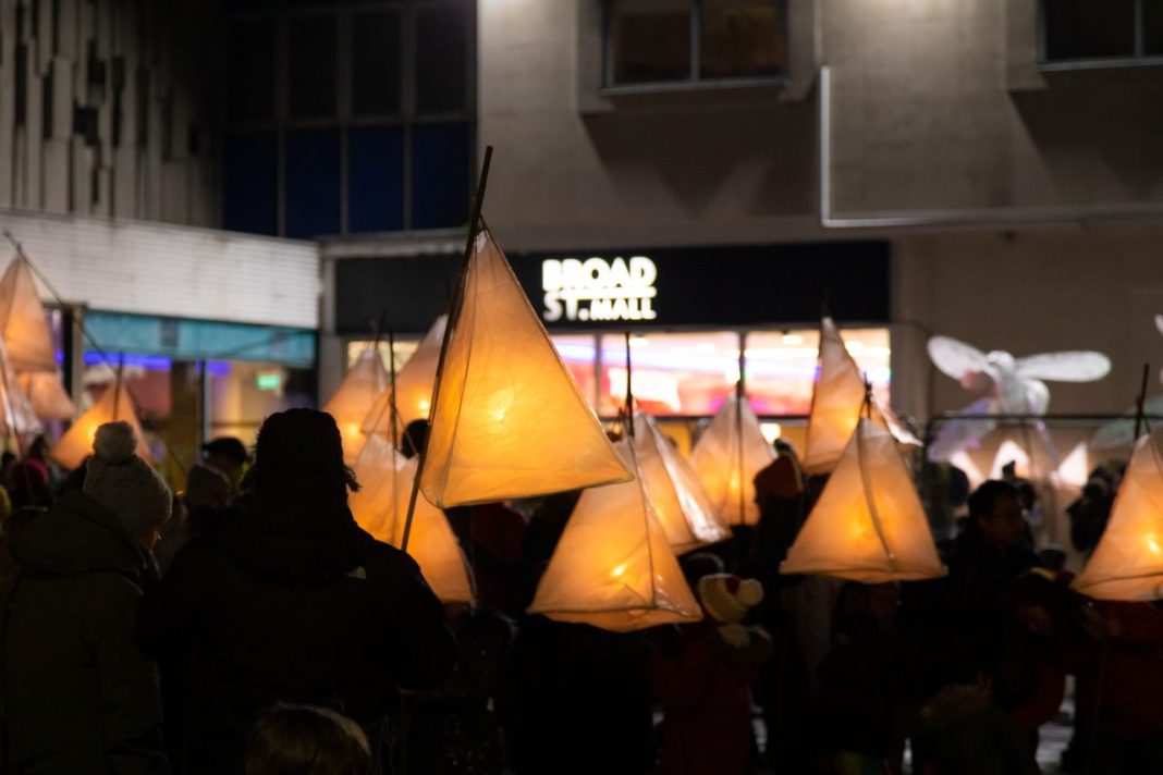 People holding tepee-style lanterns outside a sign that reads Broad St. Mall, the name of a shopping centre in Reading