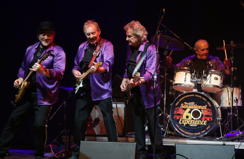 Dozy Beaky Mick and Tich are coming to The Hexagon as part of The Sensational 60s Show. They are pictured on stage with a drummer on the right. They are holding instruments