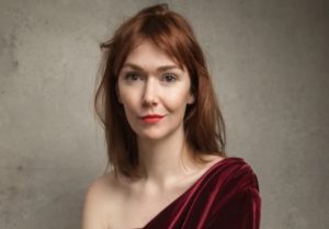 Elf Lyons head and shoulders image. She is wearing a red velvet dress on one shoulder, and has a naked neckline on the other.