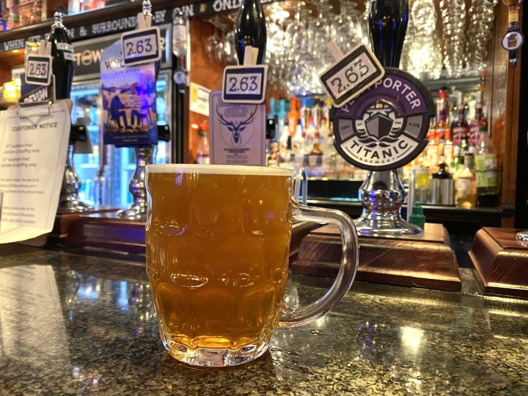 A pint of real ale on the counter of The Hope Tap in Reading. It is served in a dimpled glass. Behind the glass the pumps can be seen for four real ales. In the distance are more drinks for mixers and pint glasses