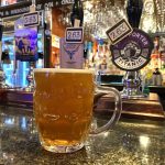 A pint of real ale on the counter of The Hope Tap in Reading. It is served in a dimpled glass. Behind the glass the pumps can be seen for four real ales. In the distance are more drinks for mixers and pint glasses