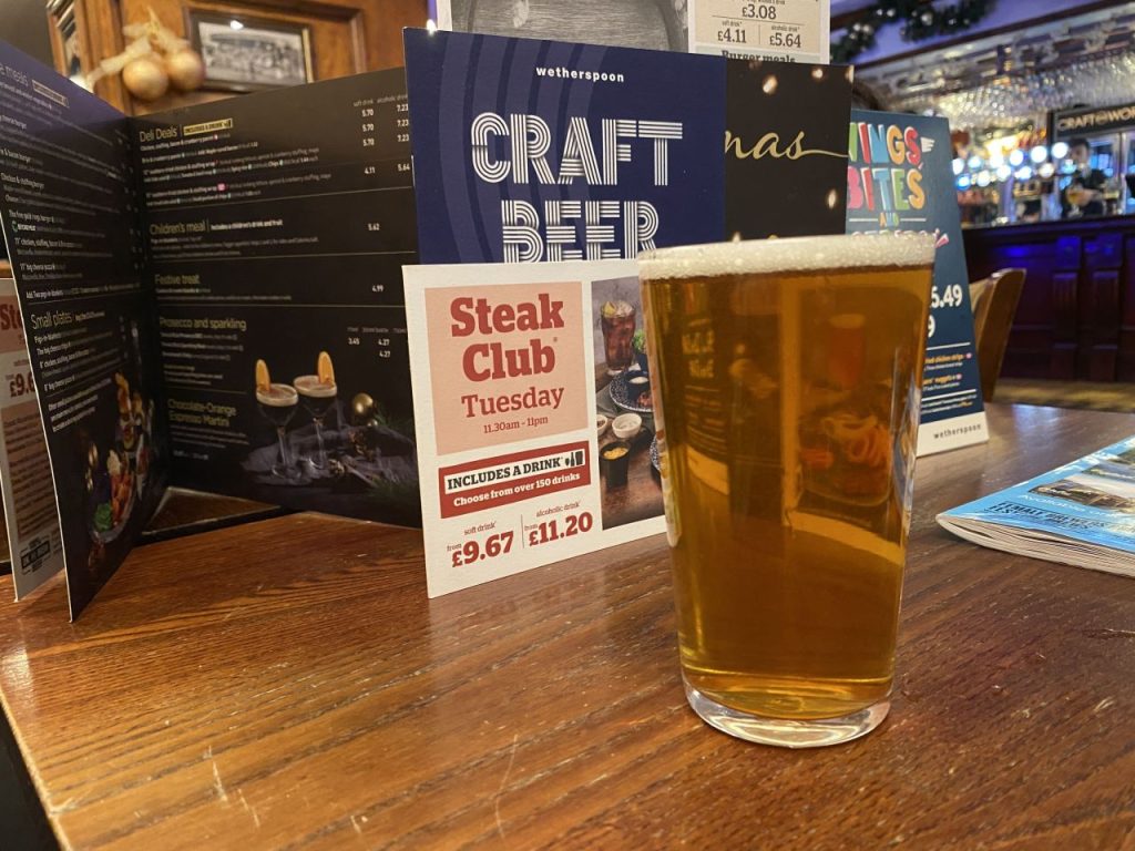 A pint of Greene King IPA on a table at The Hope Tap, surrounded by menus detailing some of the special offers available in the pub