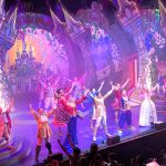Cinderella's cast celebrate the end of the show. They are standing on stage holding their arms aloft while sparklers go off in the background