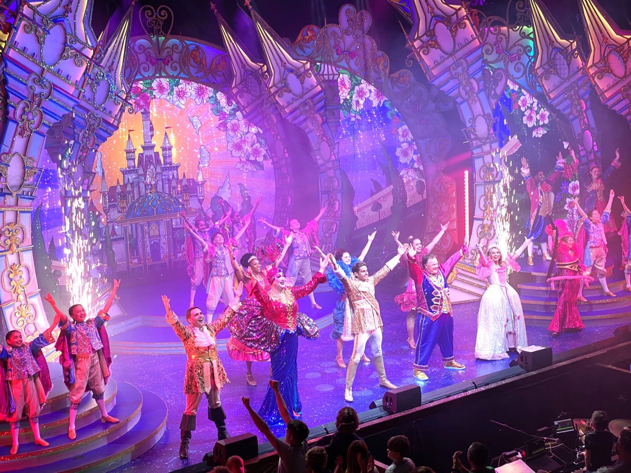 Cinderella's cast celebrate the end of the show. They are standing on stage holding their arms aloft while sparklers go off in the background