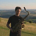 Jonny Ford holding a saxophone in a field - he is coming to South Hill Park in January 2025