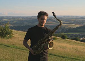 Jonny Ford holding a saxophone in a field - he is coming to South Hill Park in January 2025