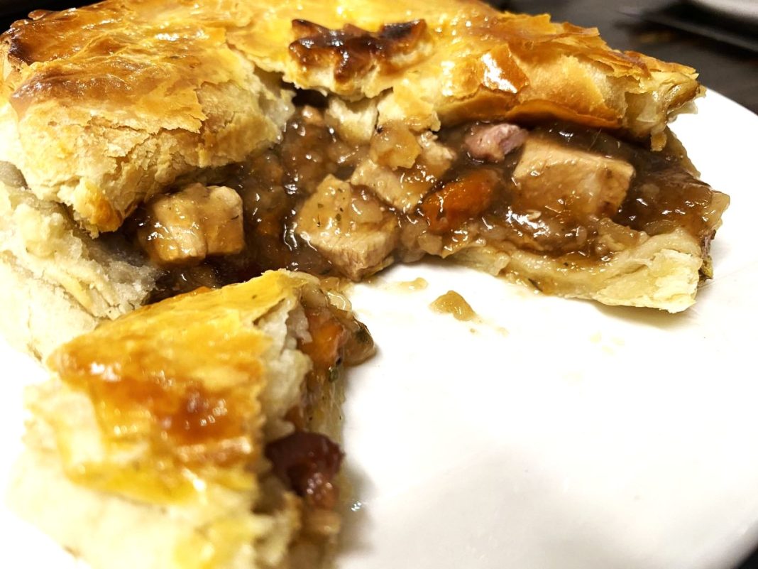 A plate showing Sweeney and Todd's Christmas pie is packed with chunks of festive meats, vegetables and cranberries. The pie has been cut open and a slice of it is in the bottom left corner of the plate