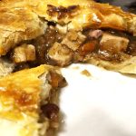 A plate showing Sweeney and Todd's Christmas pie is packed with chunks of festive meats, vegetables and cranberries. The pie has been cut open and a slice of it is in the bottom left corner of the plate