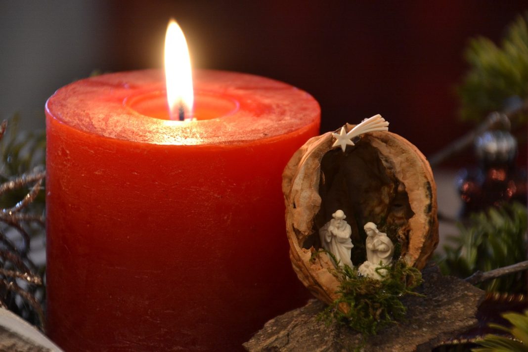 An Advent candle and a miniature crib. The candle is red and lit. The church of Christ Church in Reading is holding Advent services this Christmas