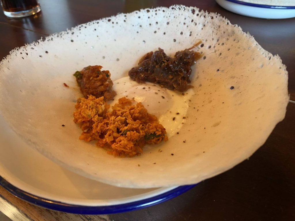 a bowl of food on a table: The Coconut Tree's hopper with an egg in the middle. A vegan version is also available