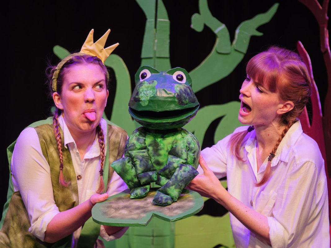 The Frog and the Princess is coming to Norden Farm - two actors, one poking their tongue out, hold a puppet frog