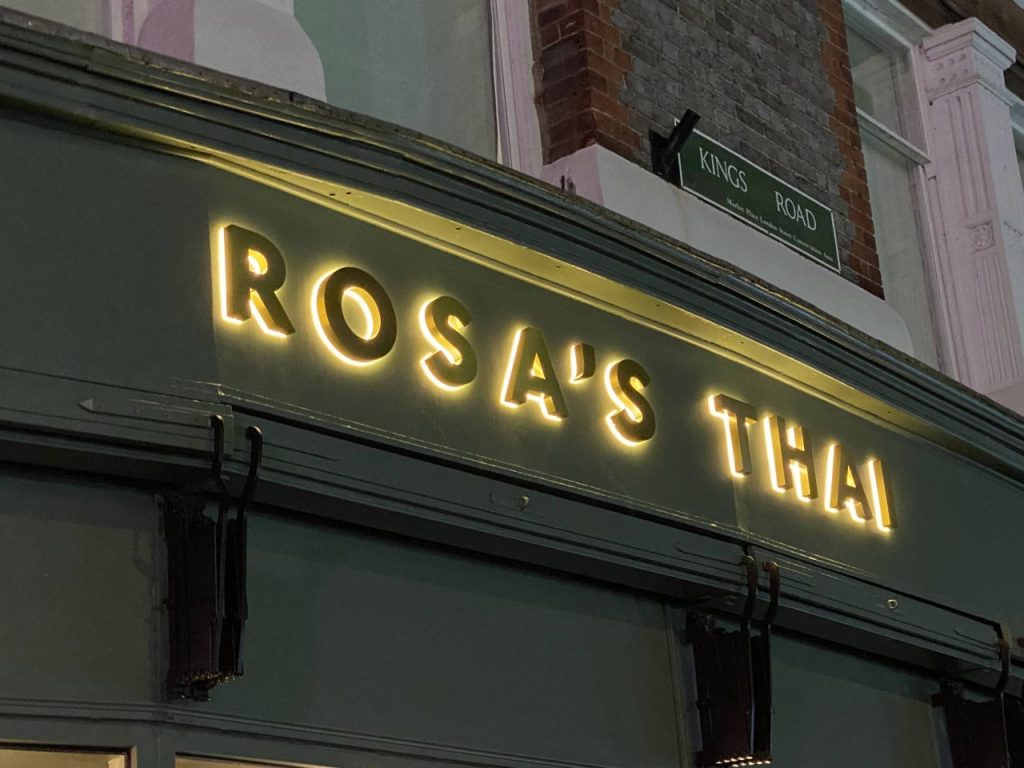 a sign on a building saying Rosa's Thai. It has been lit up