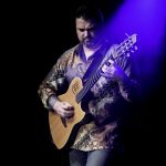Nic Meier playing a guitar under a blue spotlight