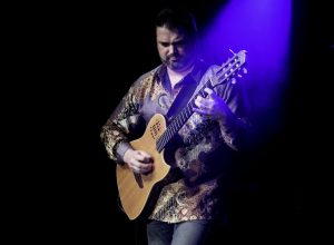 Nic Meier playing a guitar under a blue spotlight