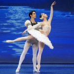 Varna International is presenting Swan Lake, a ballet. Pictured are a male and female ballet dancer on stage with a blue background