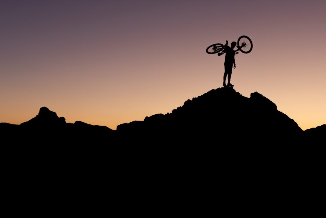 A silhouetted cyclist holding their bike aloft against a night sky, part of the The Banff Mountain Film Festival Banff Mountain Film Festival