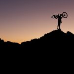 A silhouetted cyclist holding their bike aloft against a night sky, part of the The Banff Mountain Film Festival Banff Mountain Film Festival