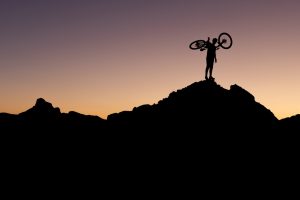 A silhouetted cyclist holding their bike aloft against a night sky, part of the The Banff Mountain Film Festival Banff Mountain Film Festival