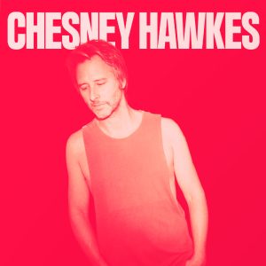 Chesney Hawkes wearing a singlet and leaning to the left. He is in a duotone print that is red. Behind him his name can be seen