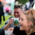 A man drinking a pint at Bracknell Ale and Cider Festival. A woman is in the foreground, she is out of focus and has a big smile on her face.