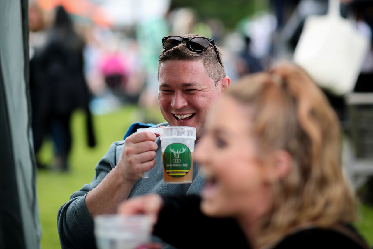 A man drinking a pint at Bracknell Ale and Cider Festival. A woman is in the foreground, she is out of focus and has a big smile on her face.