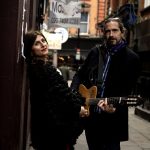 Irene Serra and Luca Boscagin standing in a street. Luca has a guitar around his shoulders. They perform The Great British Songbook