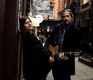 Irene Serra and Luca Boscagin standing in a street. Luca has a guitar around his shoulders. They perform The Great British Songbook
