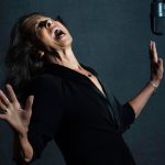 Elkie Brooks in mid song with a microphone hanging down on the right hand side. She has her arms and head up as she sings