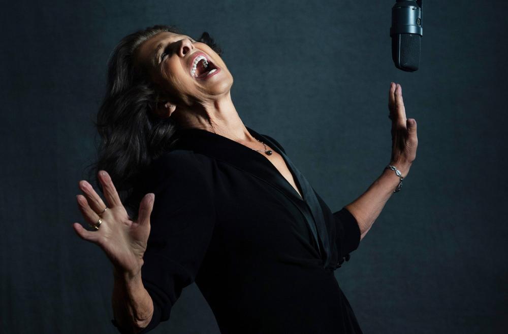 Elkie Brooks in mid song with a microphone hanging down on the right hand side. She has her arms and head up as she sings