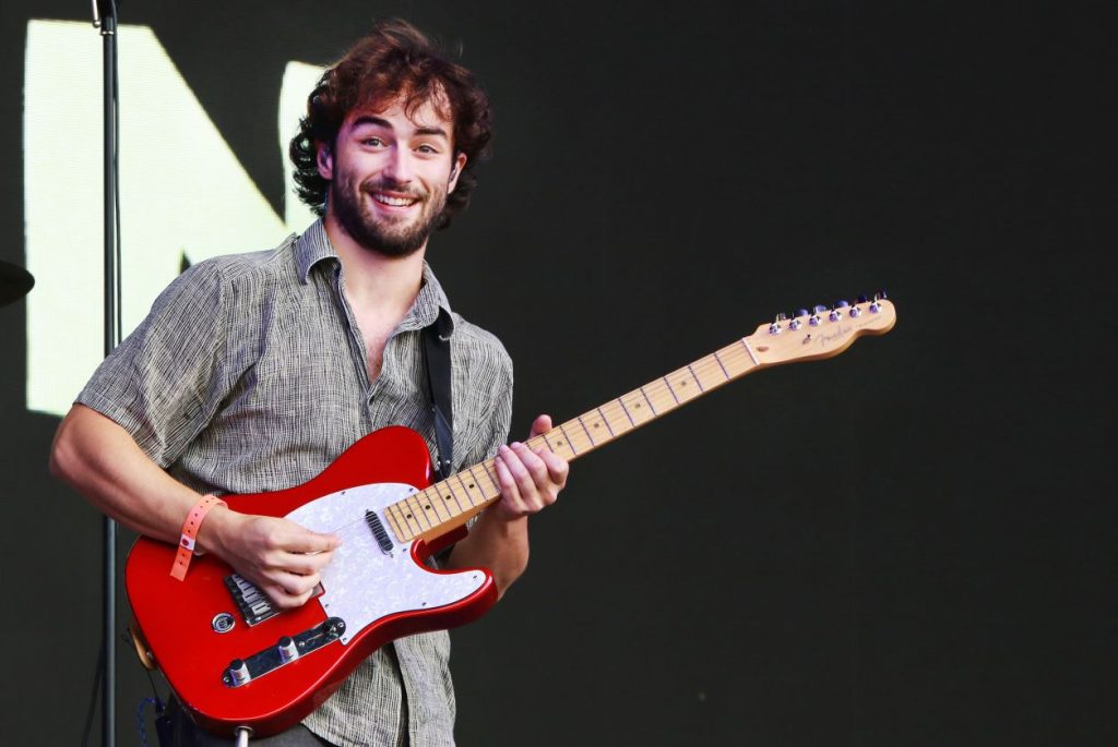 Alfie Templeman smiling and looking at the camera while playing an electric guitar