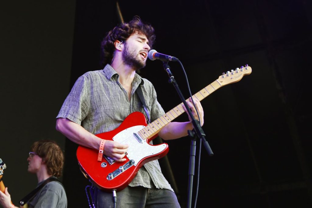 Alfie Templman in mid song. He is singing into a microphone and playing his guitar