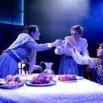 Three people around a table, the one seated is Tiny Tim