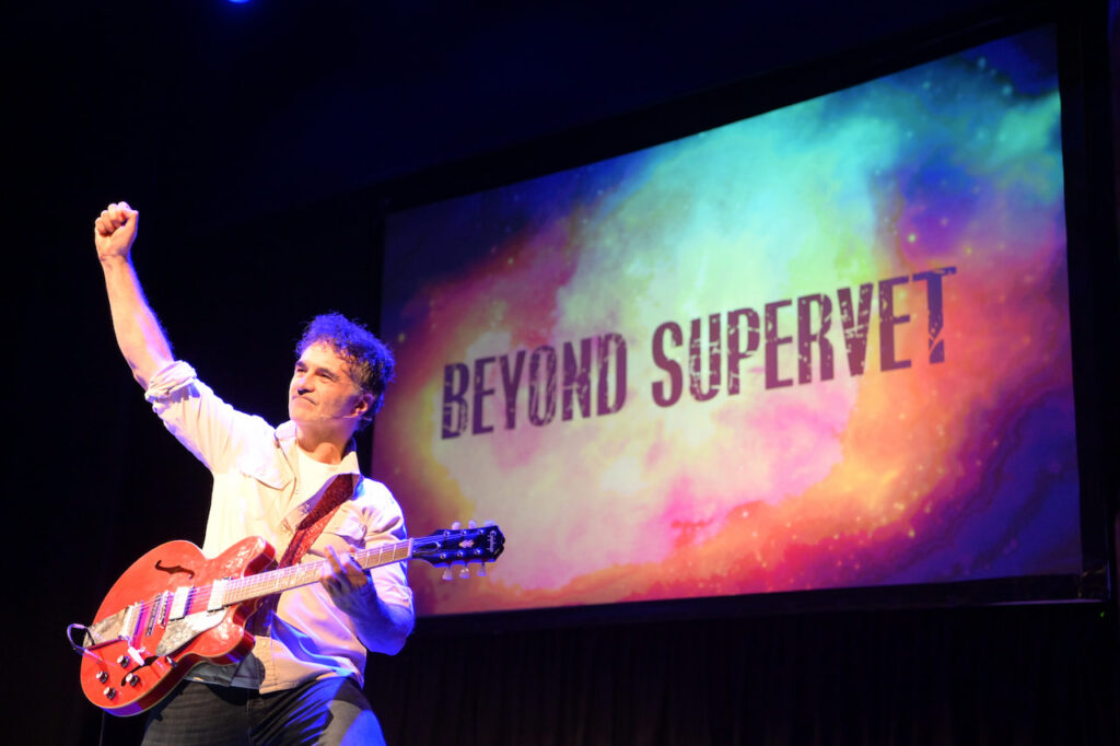 Supervet Noel Fitzpatrick holding a guitar on stage with his arm aloft