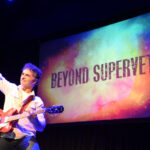 Supervet Noel Fitzpatrick holding a guitar on stage with his arm aloft