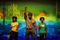 A vibrant stage scene from the musical Jamaica Love. Cast members are seen performing with energy, surrounded by a live band. The lighting is warm and evocative, capturing a moment of joyous musical celebration that represents the evolution of ska and reggae