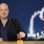Andy Parsons pushing a red button with a rocket launch behind him