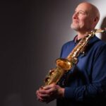 Simon Bates looking up, holding a saxophone in his hands