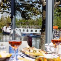 A dining table set up at Mediterranevm bray - the background is a passenger boat heading along the River Thames
